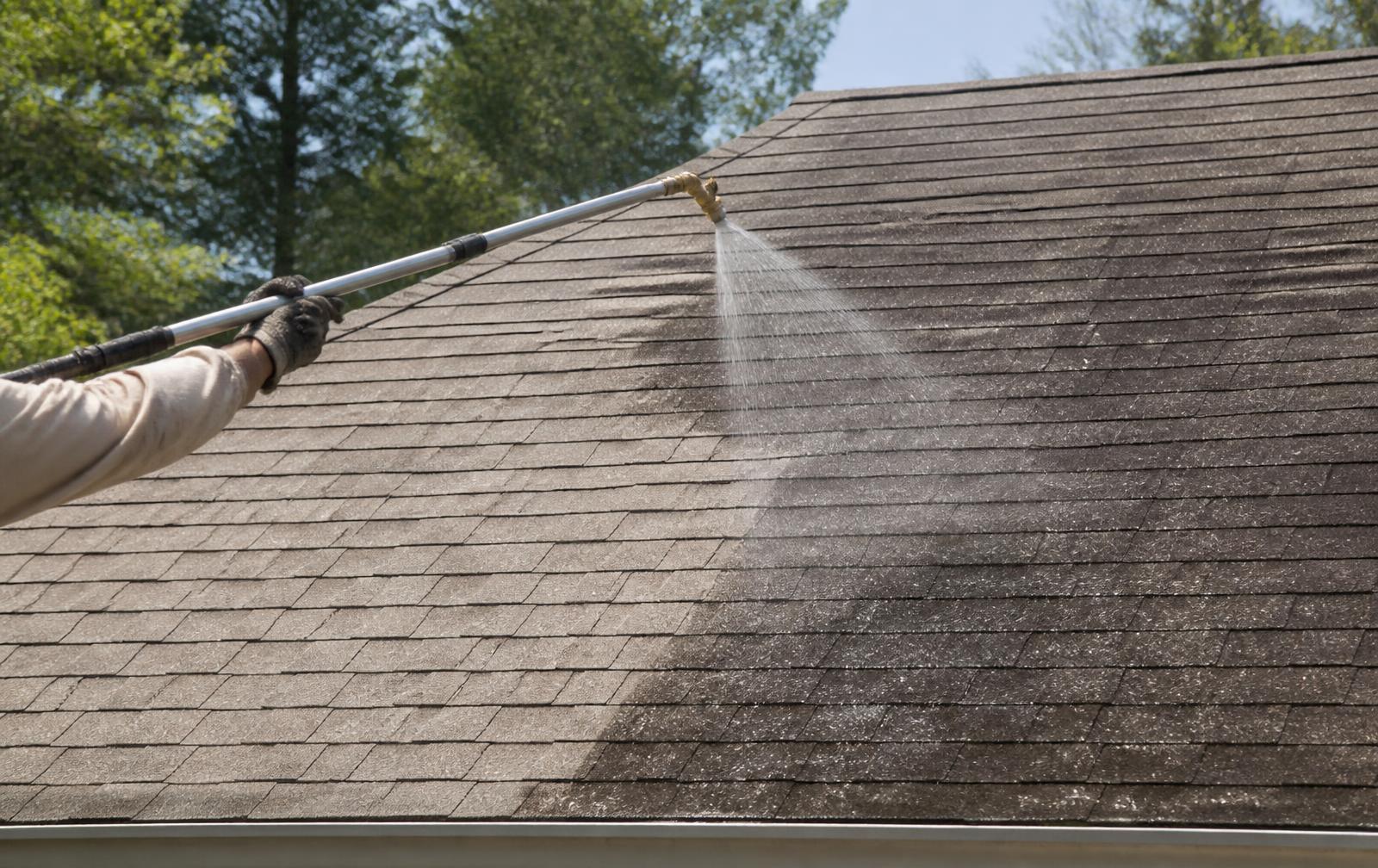 Technician soft washing black algae streaks off an asphalt shingle roof with a telescoping wand in Central Arkansas