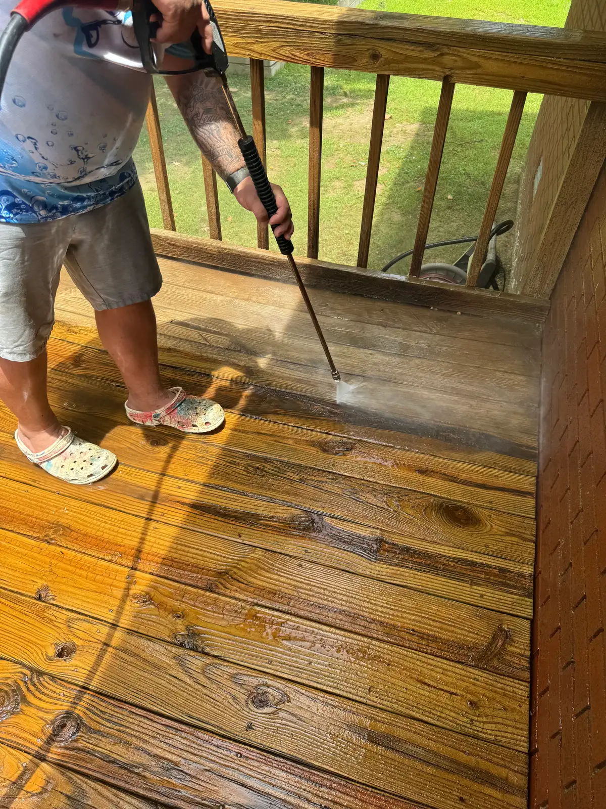 Technician pressure washing a wooden deck and railing, revealing rich clean boards beside grey weathered wood in Heber Springs, Arkansas